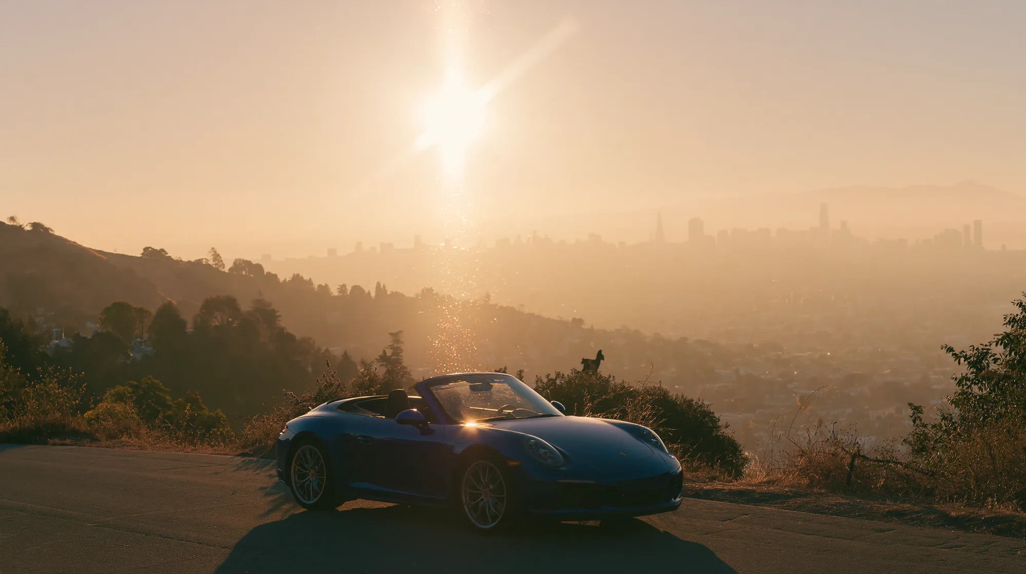 Convertible on a mountain road above a city hazy at sunset